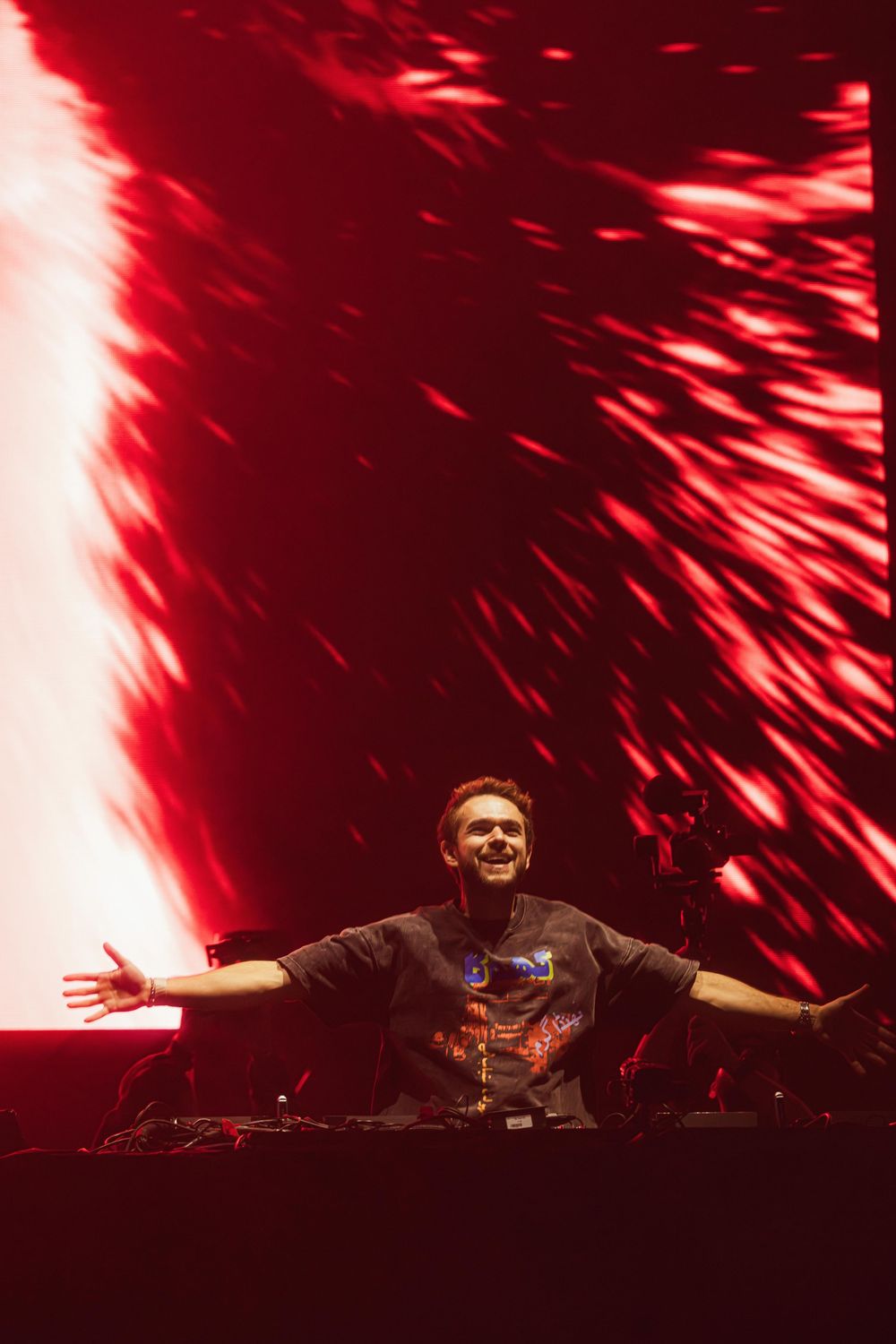 DJ performs at a concert with dramatic red lighting effects creating streaks of light across the stage during performance.