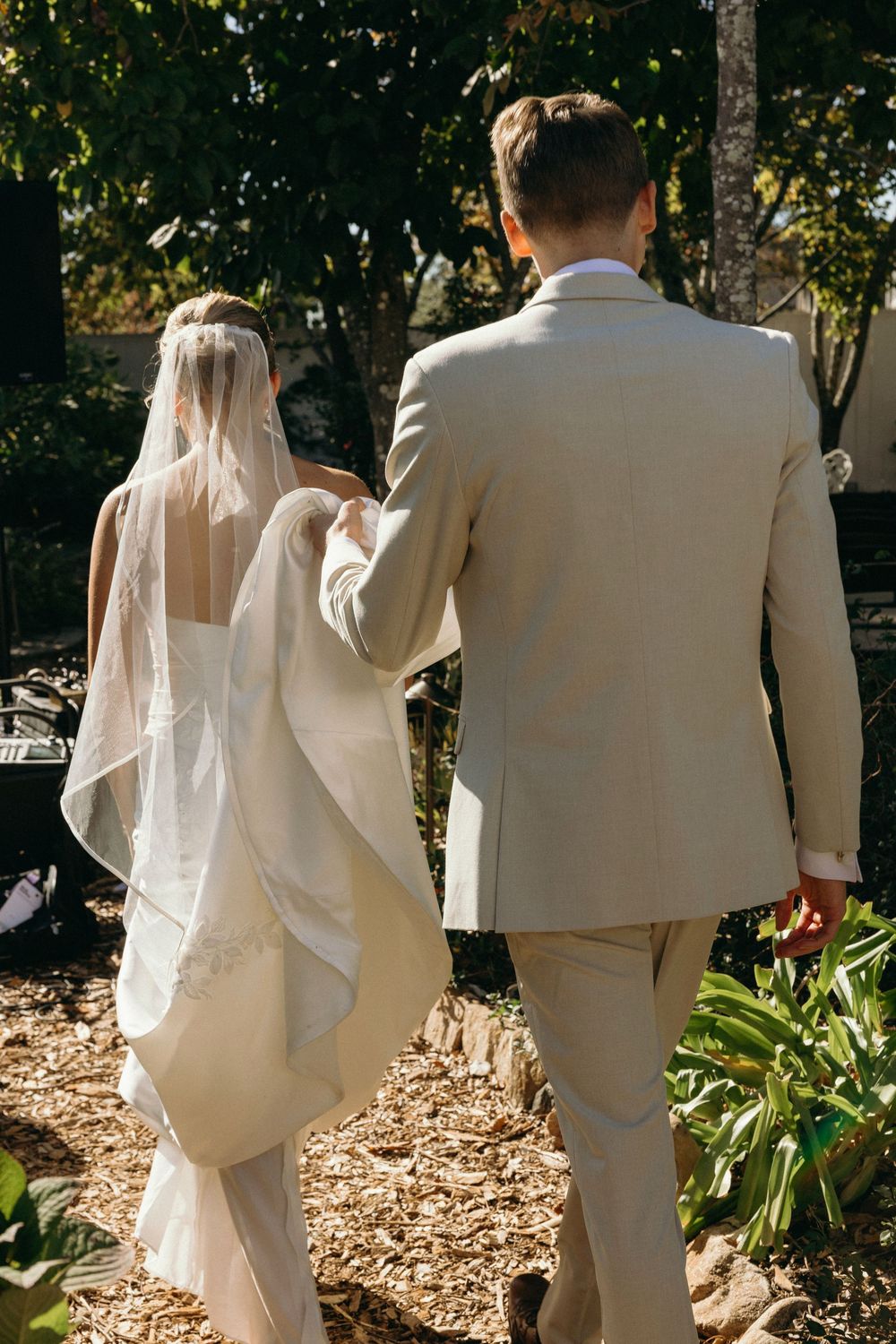 Newlyweds in white dress and beige suit walking together at Lillian Gardens in Newnan, Georgia