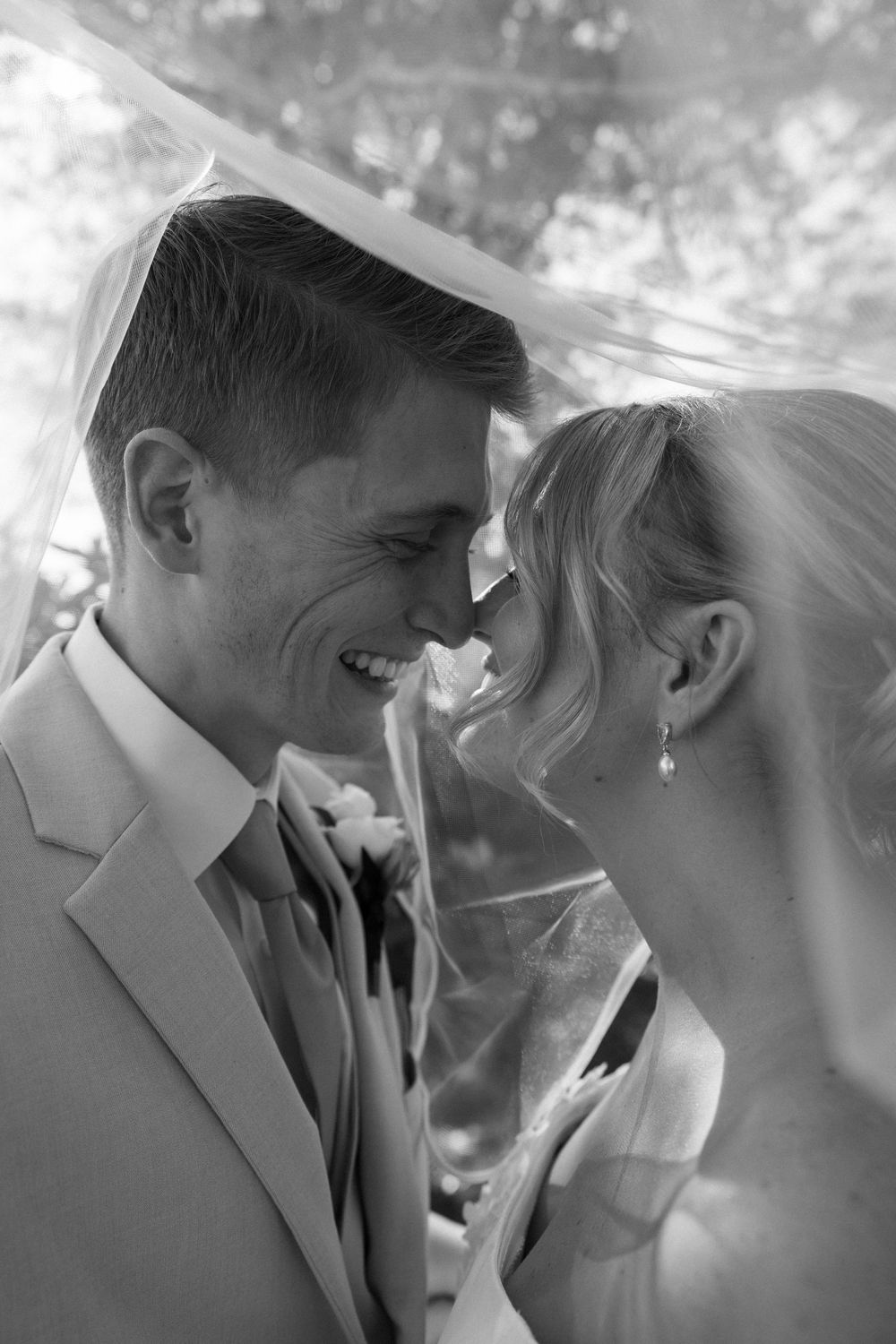 A romantic black and white wedding photograph showing a tender moment between newlyweds under a veil at Lillian Gardens in Newnan, Georgia