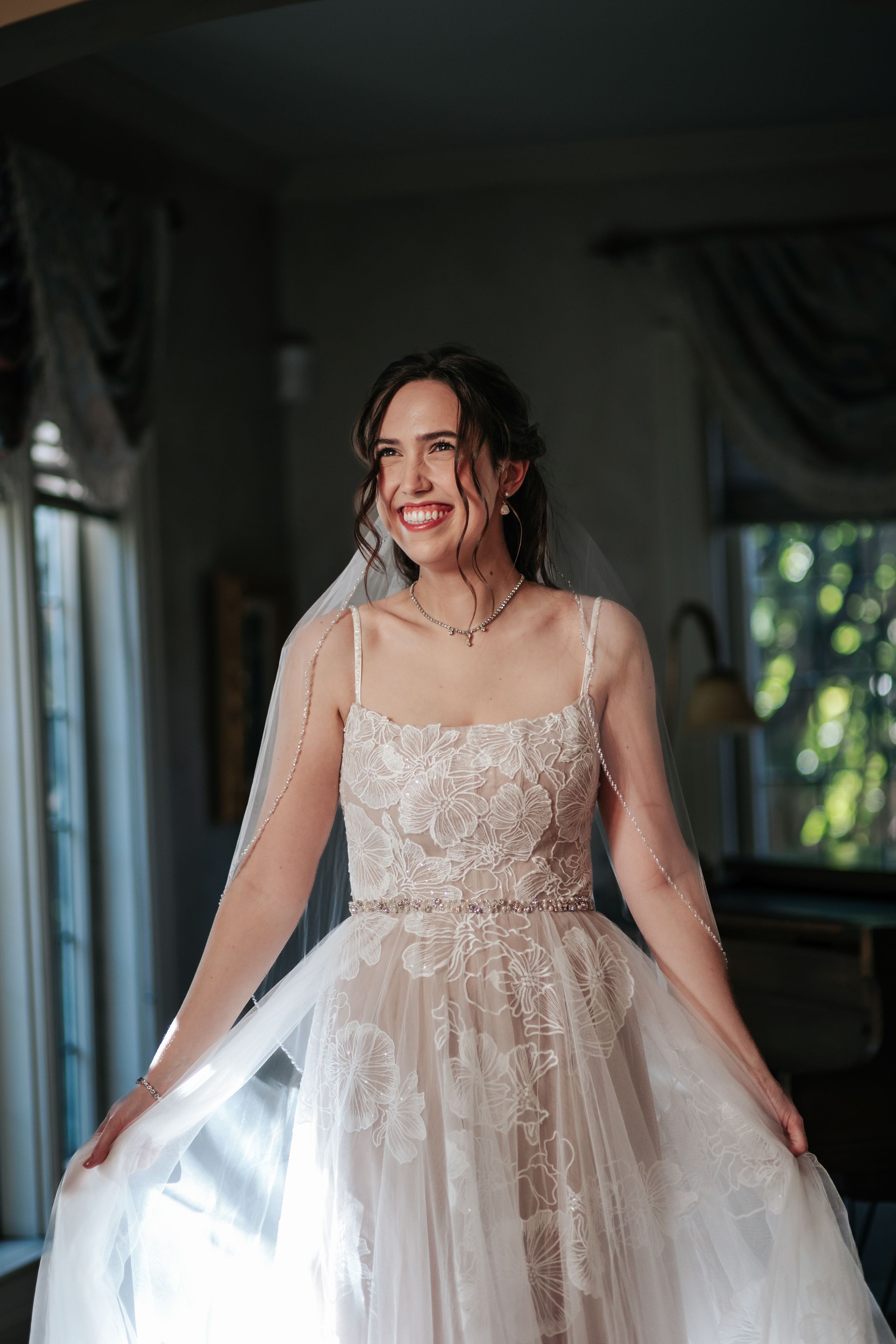 A flowing white lace wedding gown catches natural light streaming through windows.