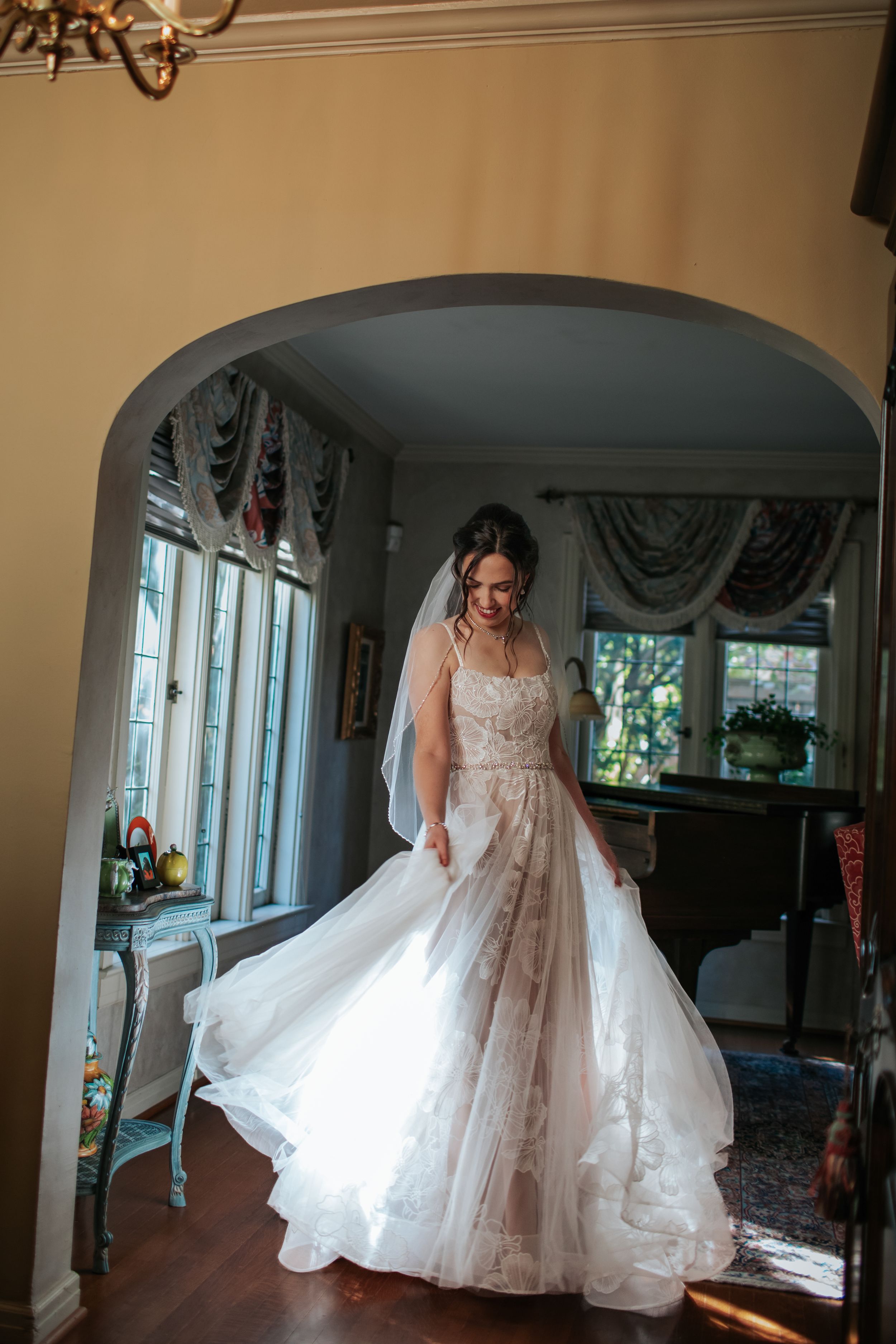 A flowing white wedding dress twirls gracefully in an elegant room with arched windows.