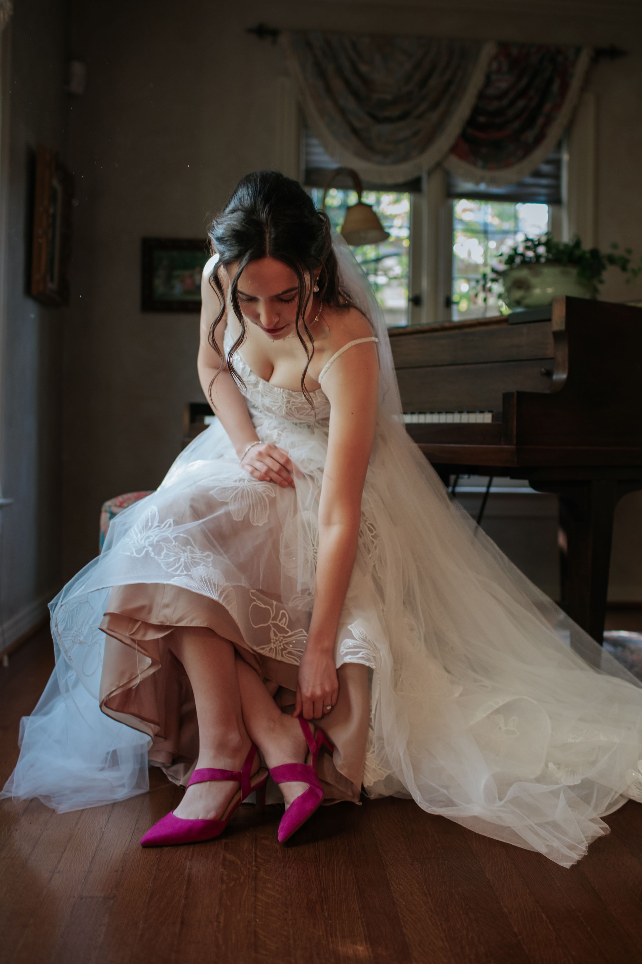 Bride in white lace dress sitting while showing off vibrant pink heels.