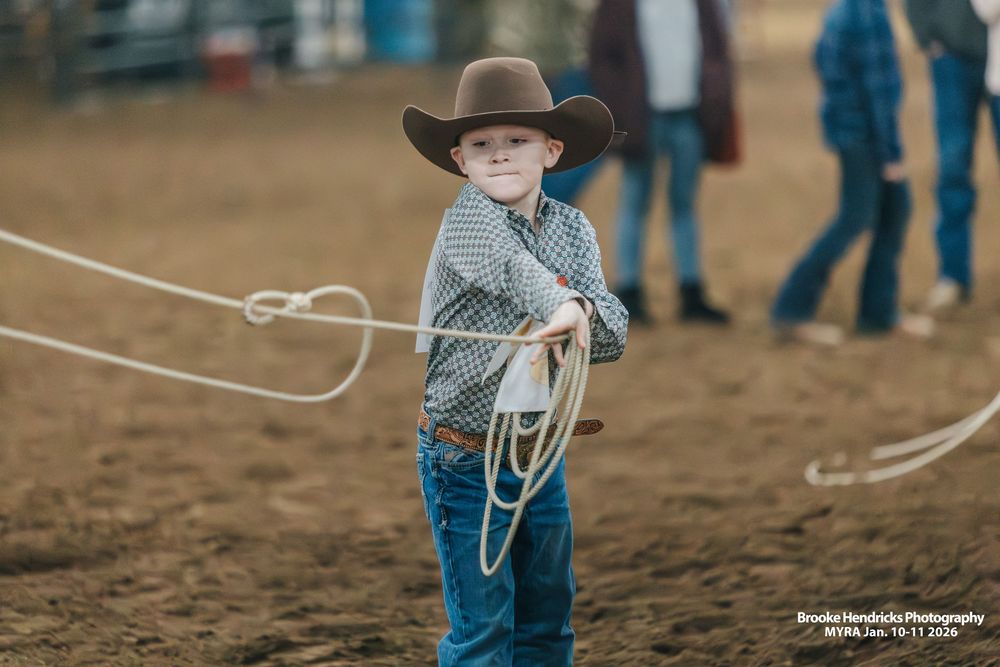 A young cowboy in denim practices roping techniques in a dusty arena.