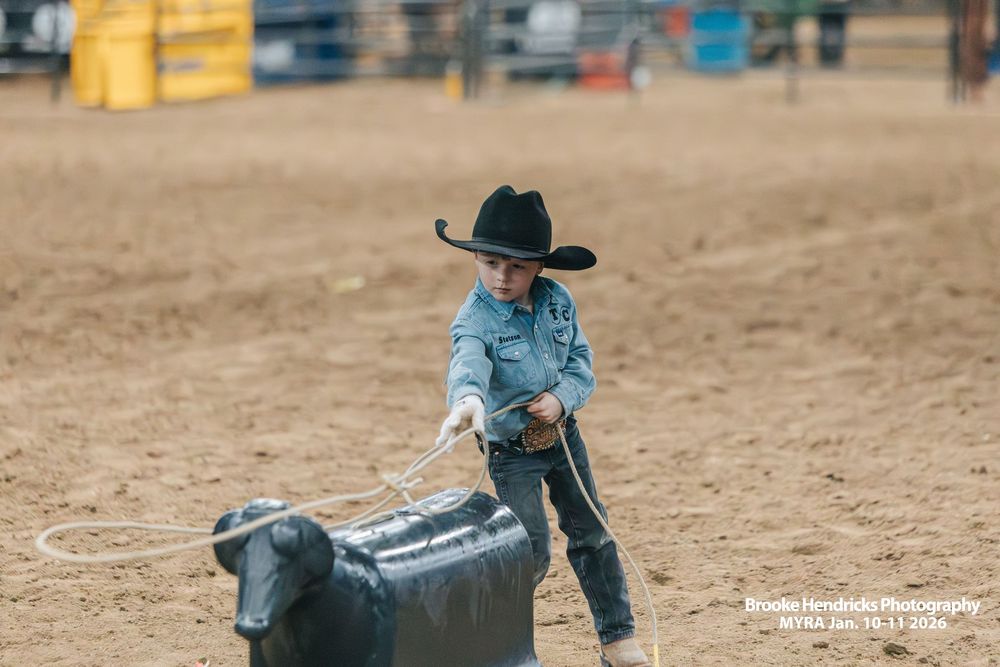 Young participant in cowboy hat practices with mechanical roping calf at rodeo training arena.