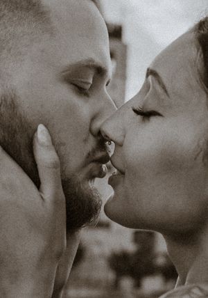 A couple shares a tender kiss in a sepia-toned close-up, the man with a beard gently holding her face.