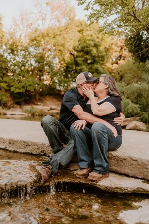 A romantic couple shares a tender kiss while sitting on rocks near a stream during golden hour.