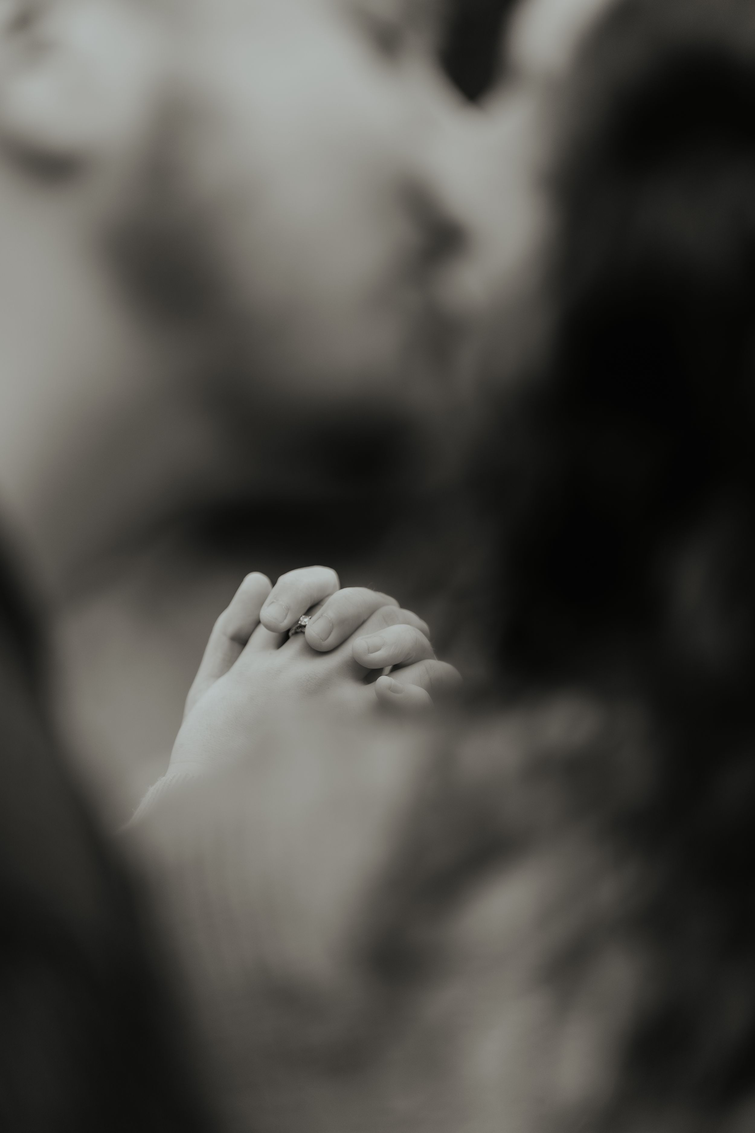 A close-up artistic black and white portrait showing hands gently touching in an intimate moment.