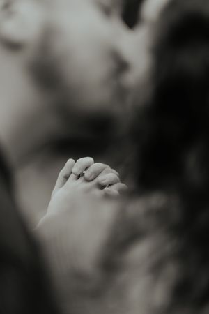 A close-up artistic black and white portrait showing hands gently touching in an intimate moment.