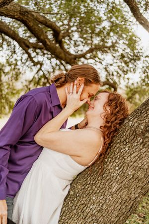 Romantic couple shares intimate moment under sprawling oak tree.