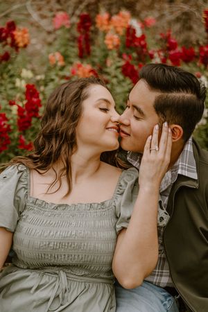 Couple sharing a romantic almost-kiss among vibrant red and orange flowers during an outdoor engagement photo session.