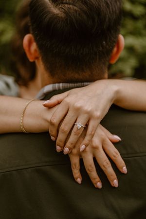 Close-up of a woman's hand with a diamond engagement ring resting on her partner's shoulder during a photo shoot.