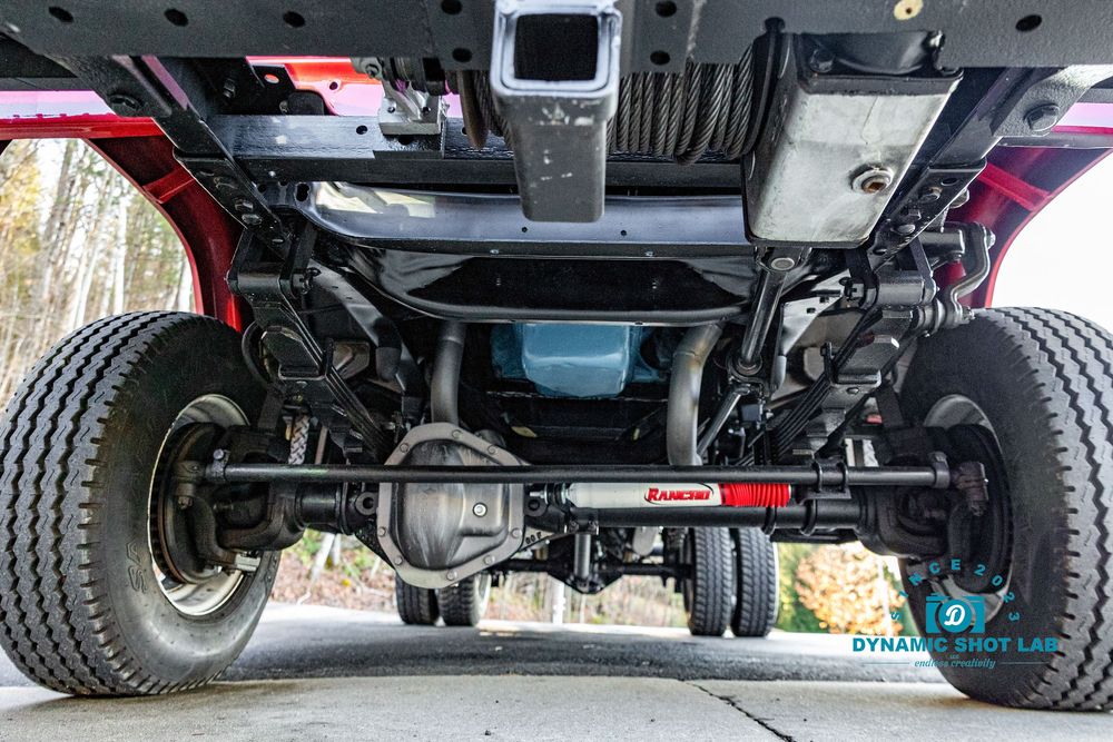 Undercarriage view of a red truck showing rear axle, suspension components, and Rancho shock absorbers.