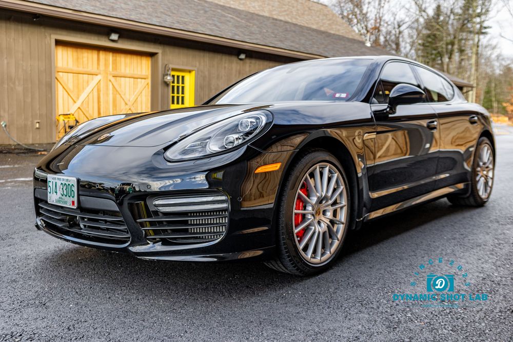 Black Porsche Panamera Turbo parked on gravel driveway with red brake calipers and Vermont license plate.