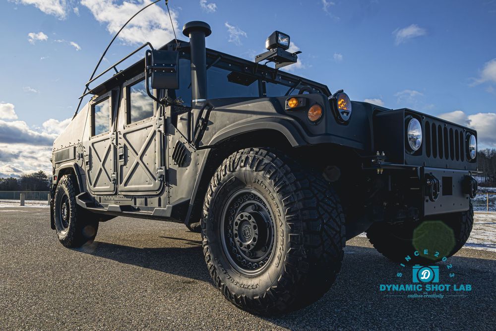 Military green Humvee HMMWV parked outdoors on a clear day, showcasing rugged off-road tires and tactical design.