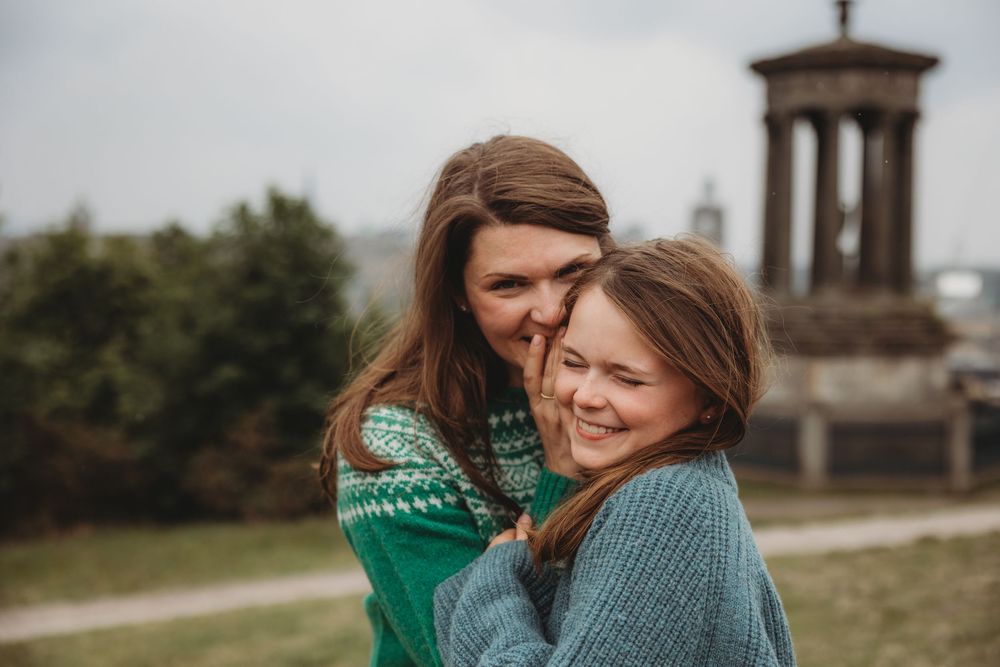 Couple in matching green sweaters share tender moments at scenic overlook in Edinburgh.