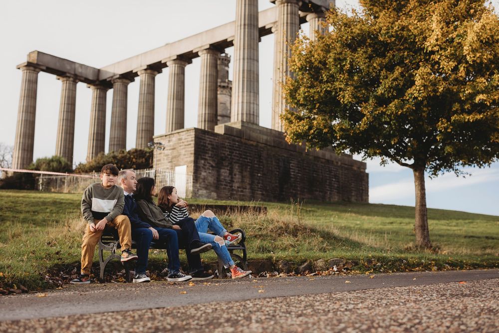 Friends relaxing on blankets at sunset overlooking a scenic hilltop vista with autumn trees and columns.