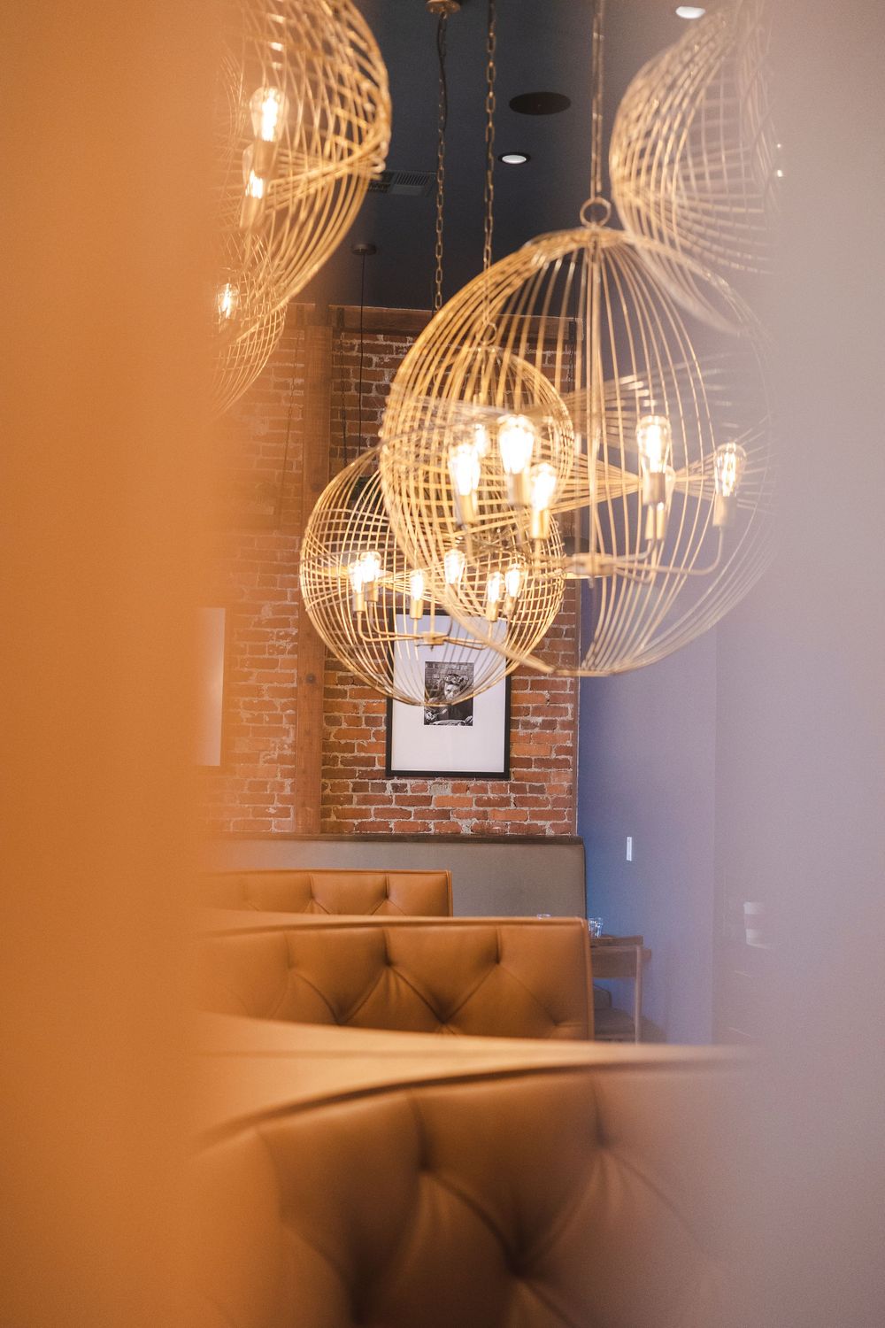 Elegant wire globe pendant lights cast warm illumination over brown leather banquettes in an upscale restaurant interior.