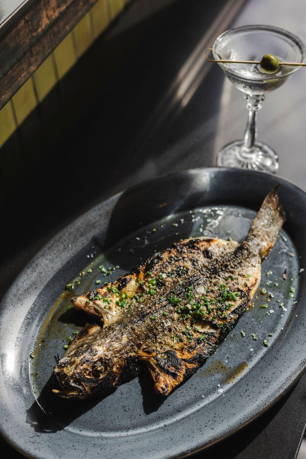 Grilled fish fillet garnished with fresh herbs served on a dark plate with elegant plating.