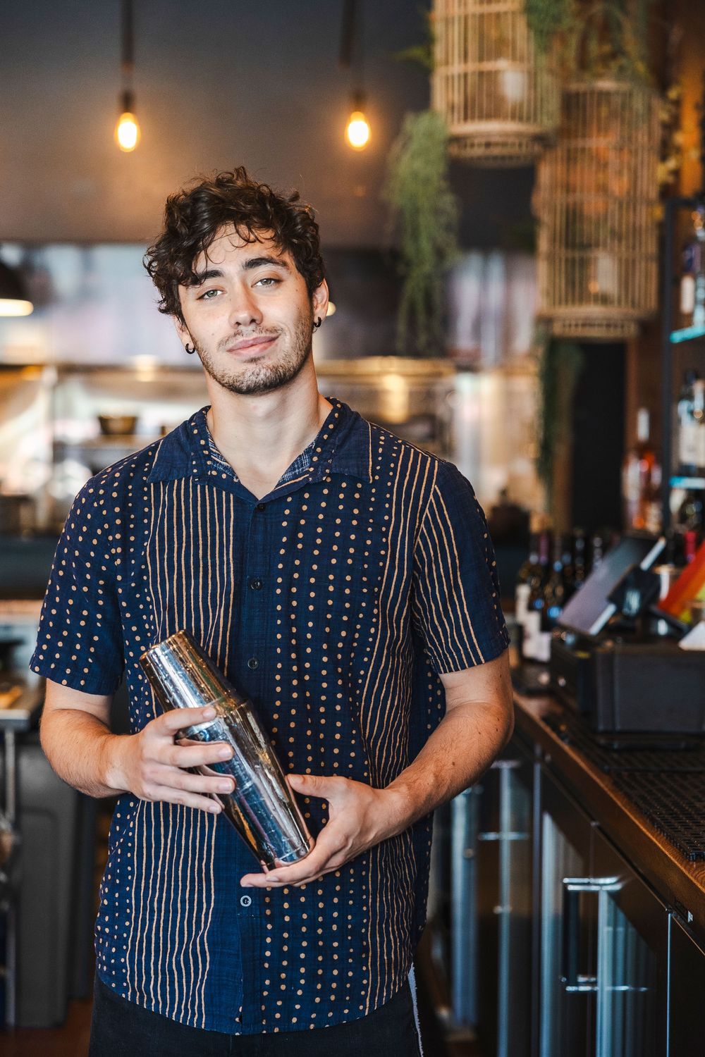 Person in a navy polka dot and striped shirt demonstrating drinks at a bar counter.