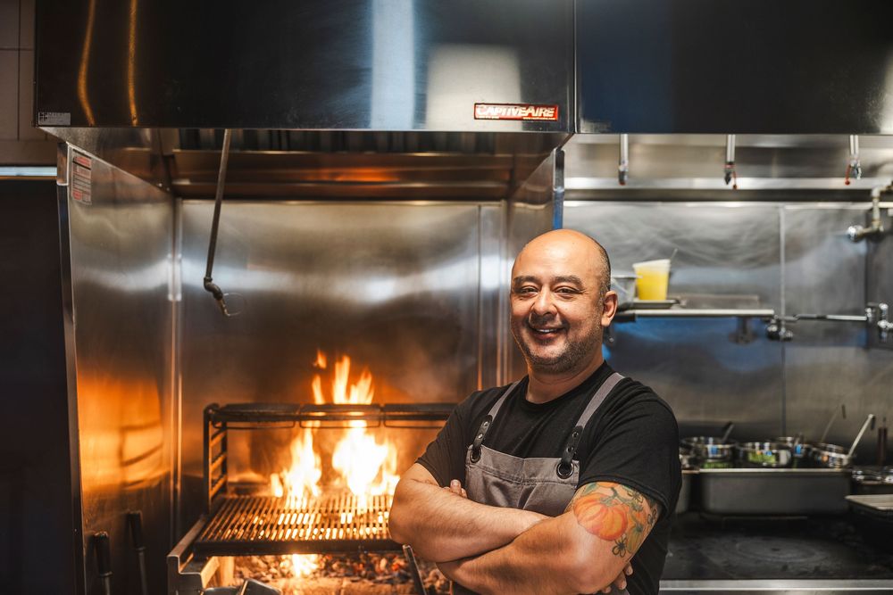 Professional chef working in a commercial kitchen with flames visible from cooking station.