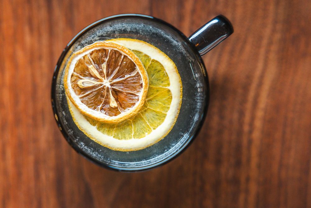A sliced lemon garnish on a wooden surface shown in four sequential photos demonstrating its placement.
