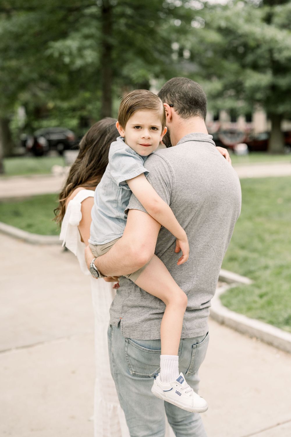 A series of candid family moments showing a parent carrying a child while walking through a park on a sunny day.