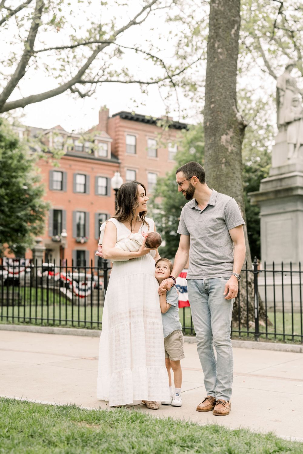 A series of candid family moments captured in a park setting with brick buildings in the background.