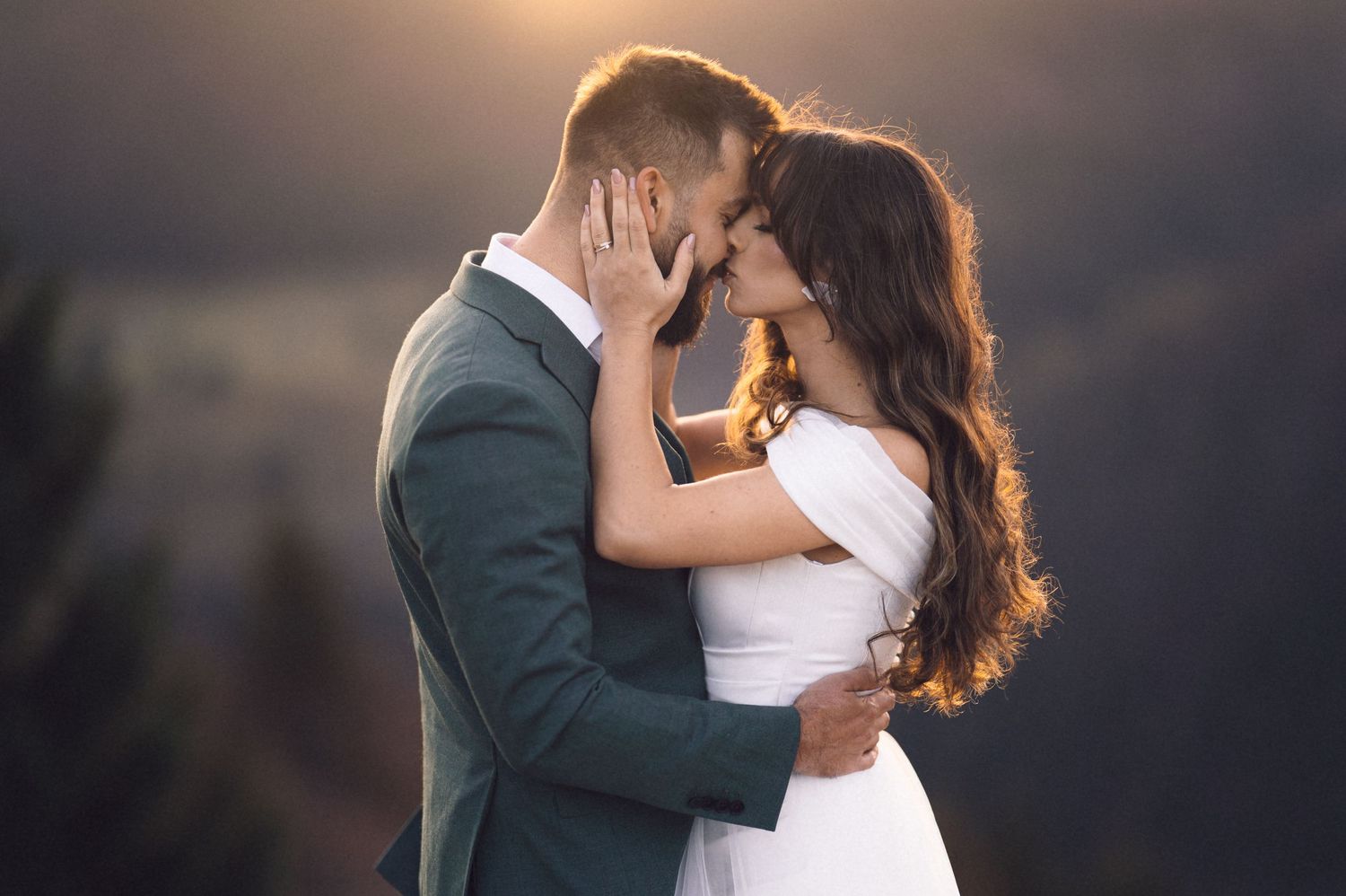 A romantic sunset wedding photo of a couple embracing with mountains and golden light in the background.