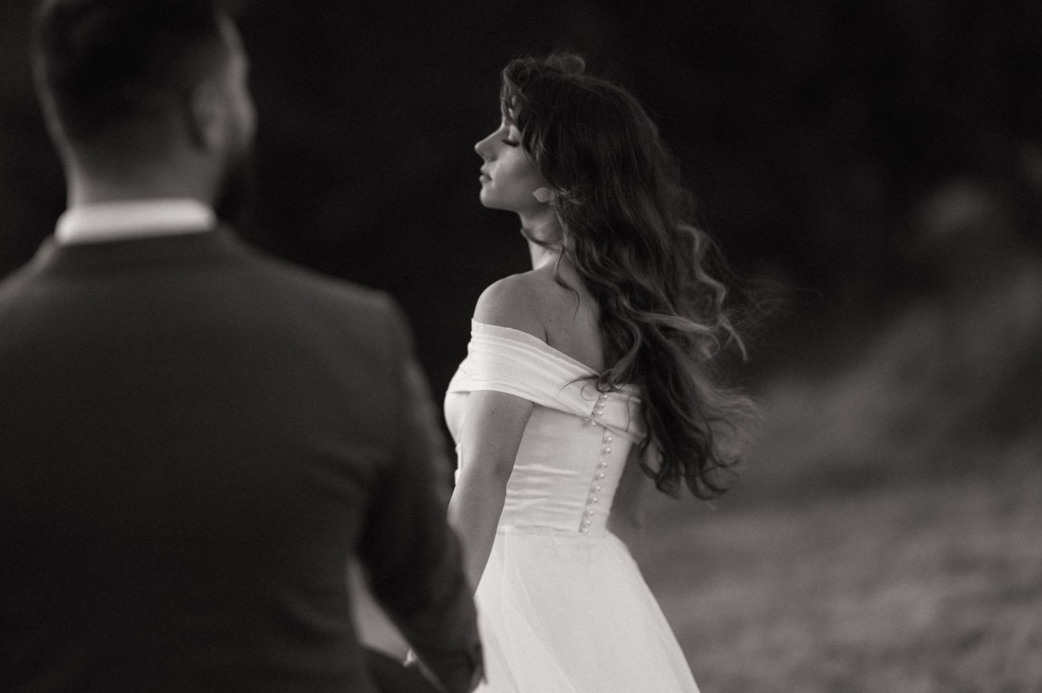 Black and white photo of a bride in an off-shoulder wedding dress spinning with her hair flowing in the wind.