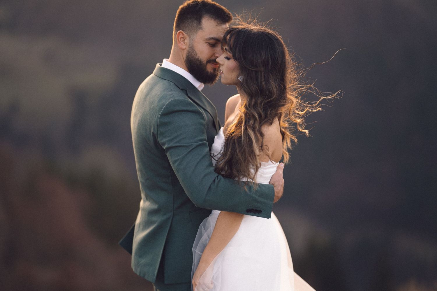 A romantic couple embraces during a misty outdoor wedding photoshoot with dramatic lighting and natural scenery.