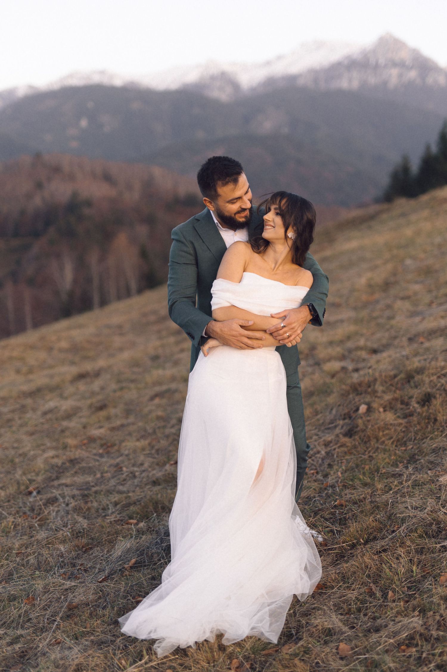 A couple shares a romantic moment on a mountainside at sunset in their wedding attire.