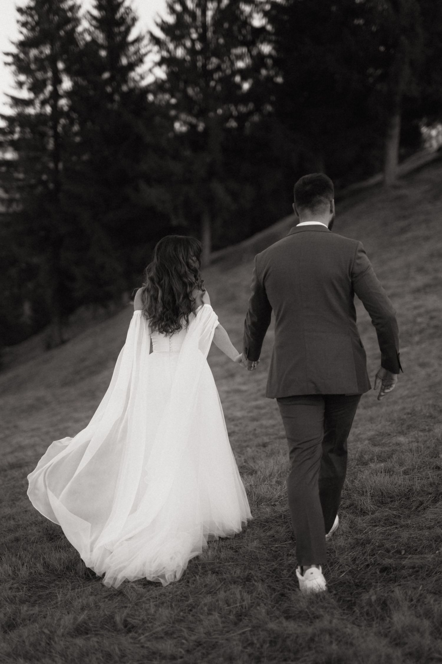 A bride and groom walk up a grassy hillside in a series of black and white wedding photos showing flowing white dress.