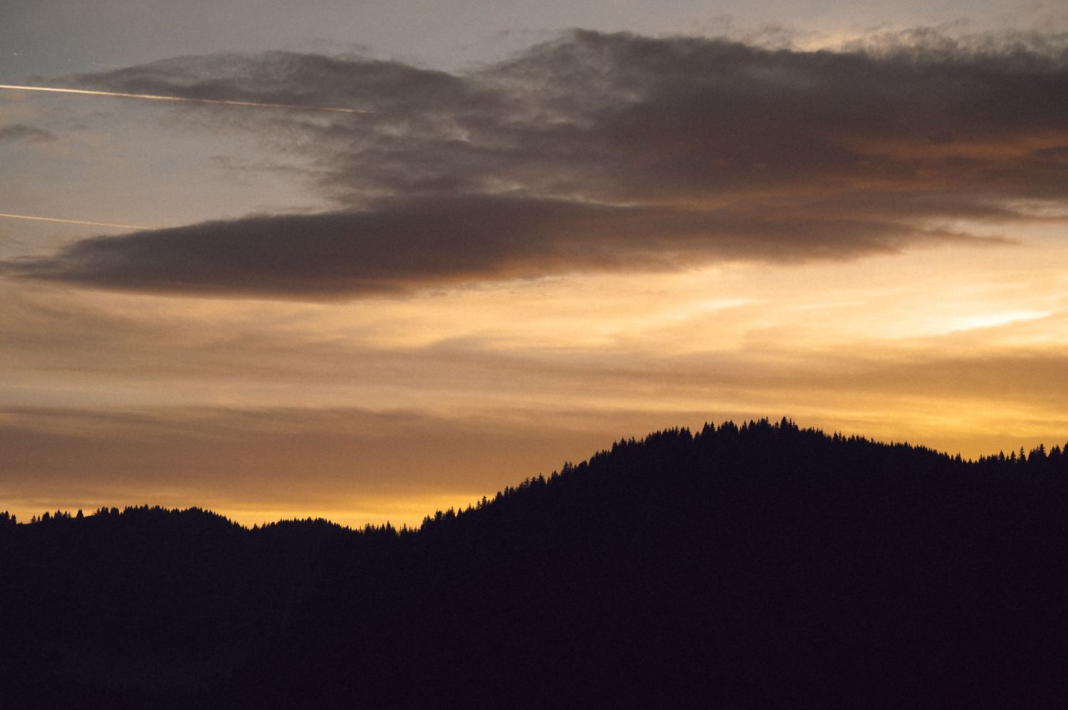 Silhouetted mountain ridge against a dramatic orange and purple sunset sky with wispy clouds.