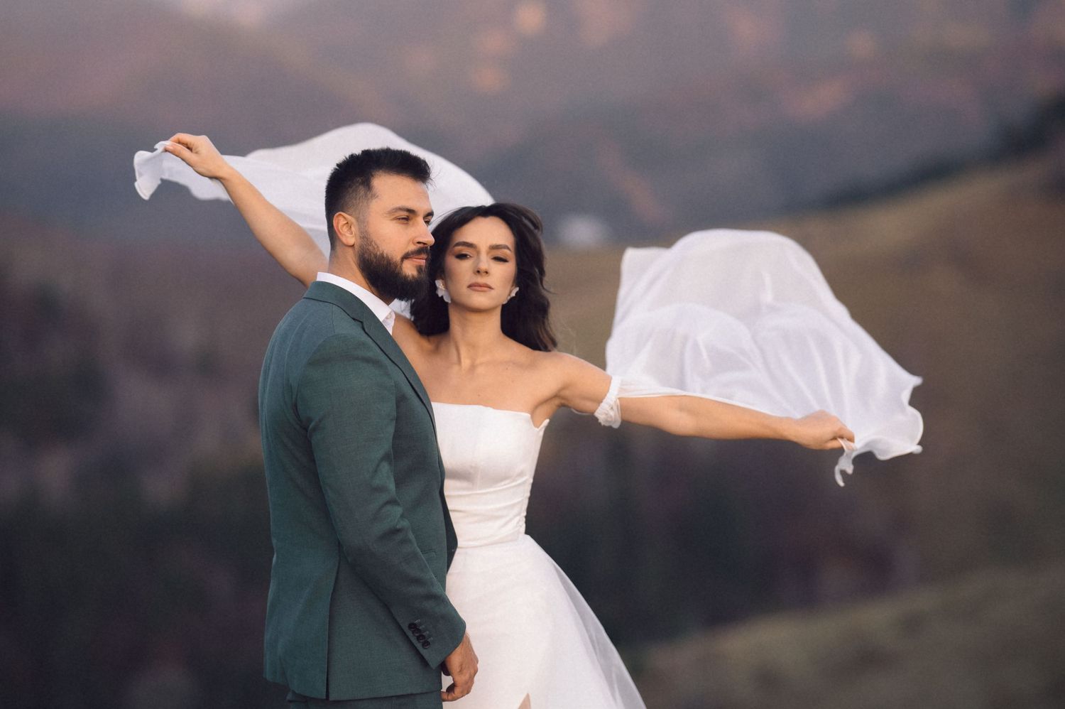 A couple in wedding attire dances together against a scenic mountain backdrop at sunset.