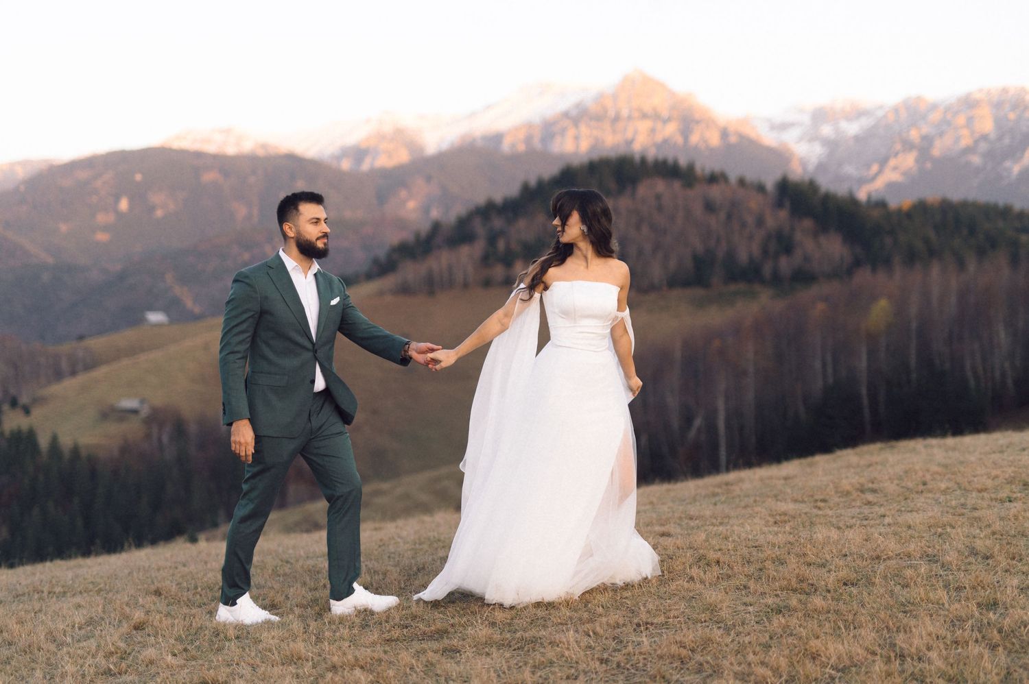 Newlywed couple poses in front of majestic mountain landscape during sunset at their outdoor wedding ceremony.