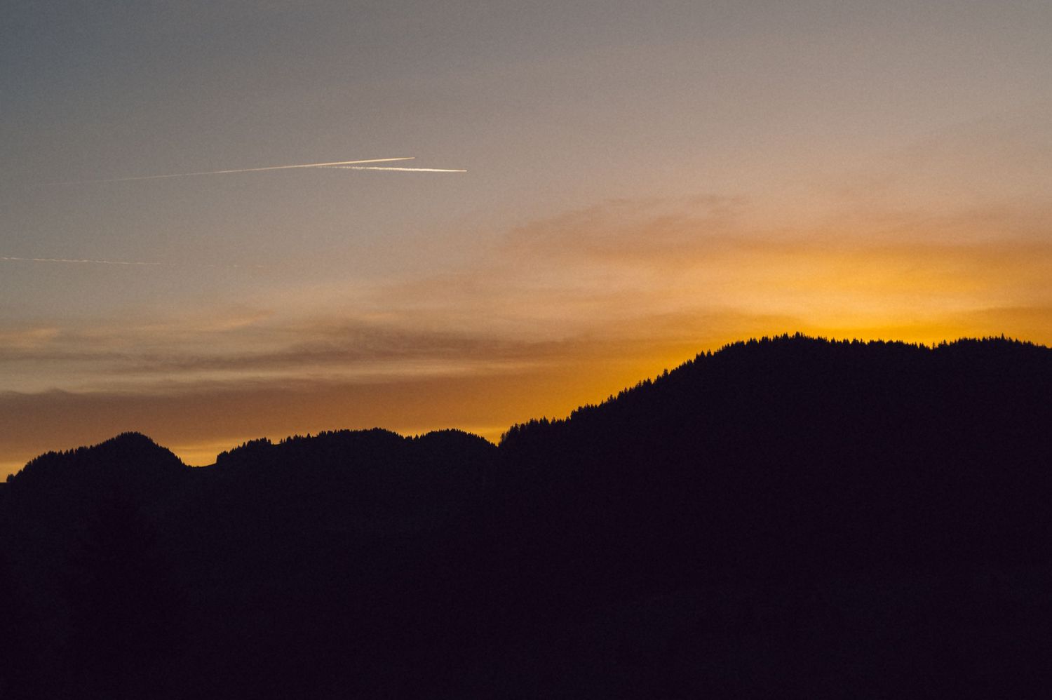 Mountain silhouettes against a vibrant orange and purple sky during sunset create a dramatic panoramic landscape.