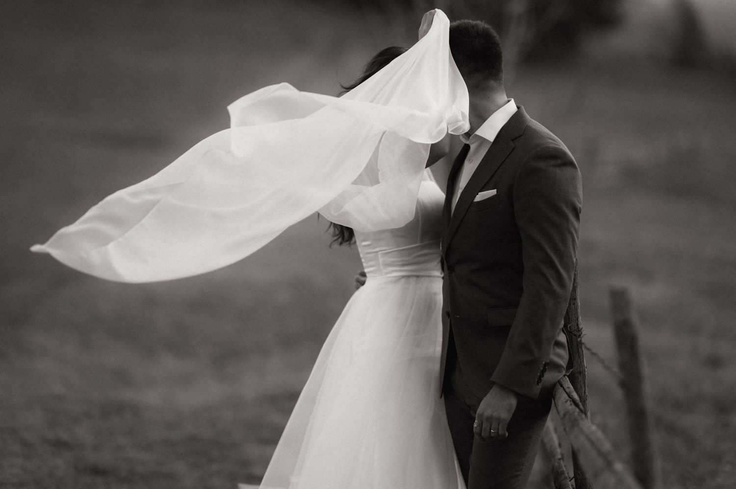 A flowing white wedding veil billows gracefully in the wind against a dark background in black and white.