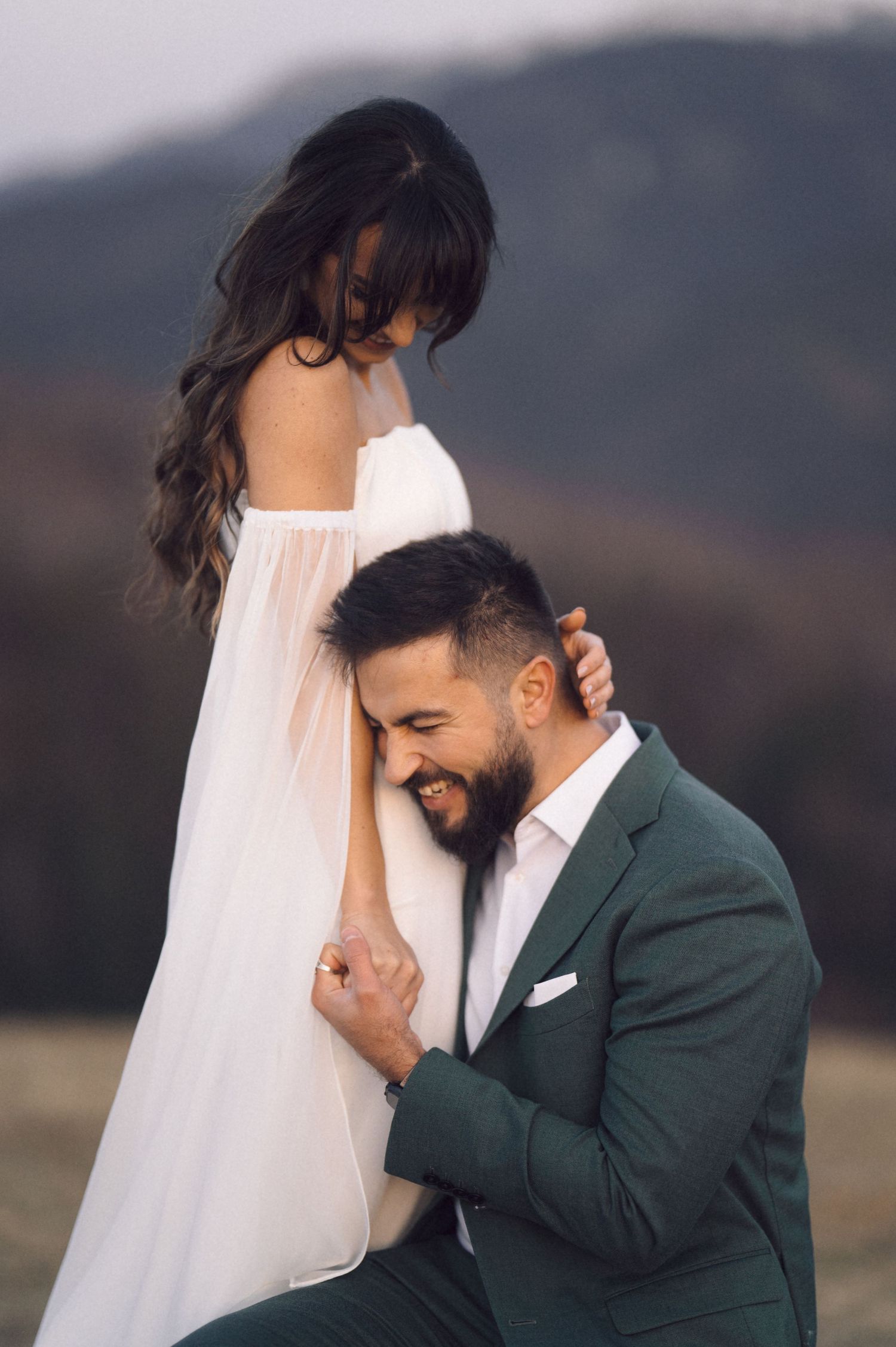 A joyful couple shares an intimate moment during their wedding photoshoot in front of a mountainous landscape.