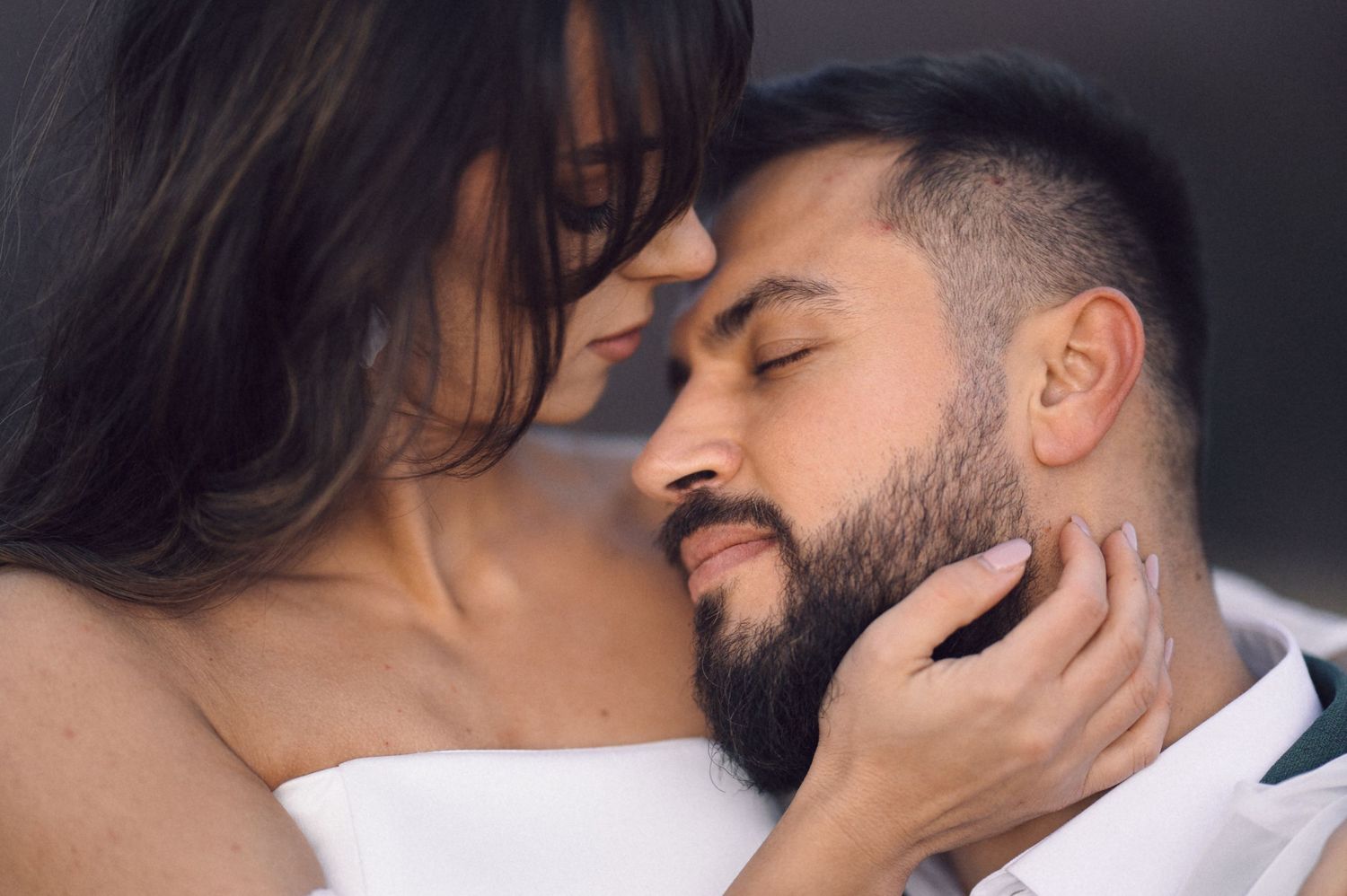 Two people share an intimate romantic moment with a tender kiss and embrace in a dimly lit setting.