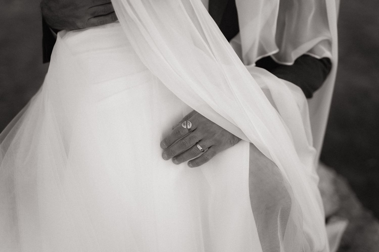 A black and white photo of a bride in a flowing white wedding dress walking through a doorway.