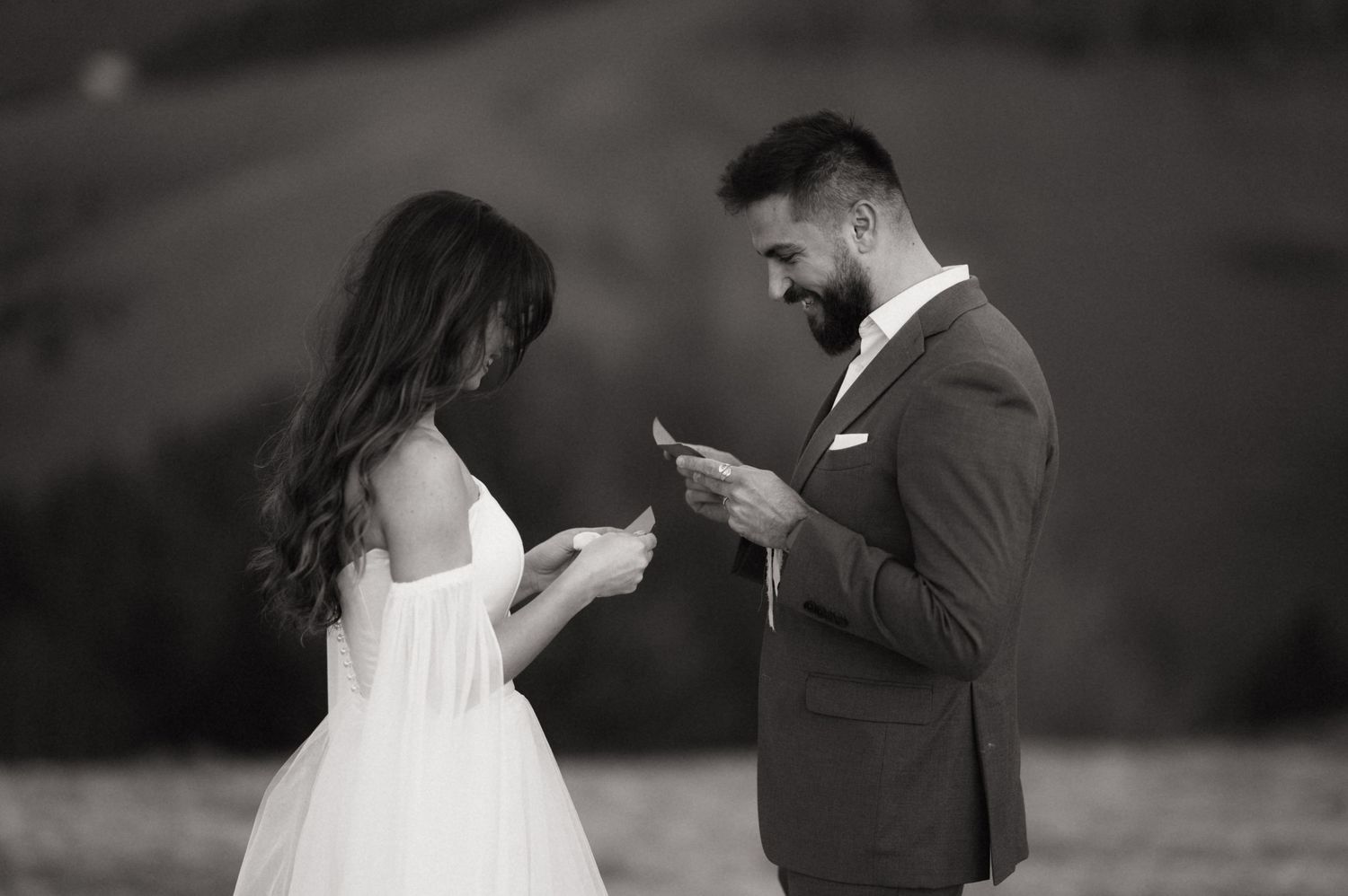 A bride and groom exchange vows while reading from their phones during an outdoor wedding ceremony.