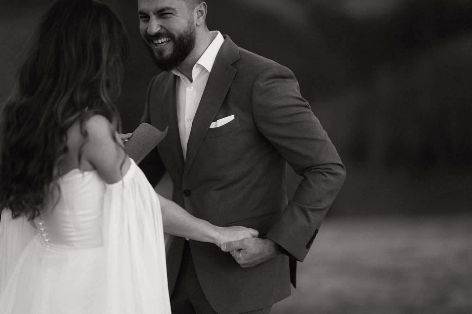 Black and white wedding photo showing a joyful moment between a bride in white dress and groom in suit.
