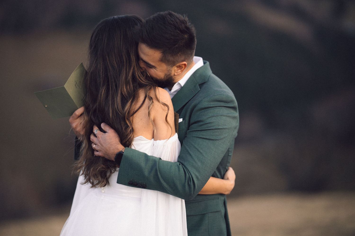 A romantic couple in wedding attire embrace in a scenic outdoor setting during their special day.