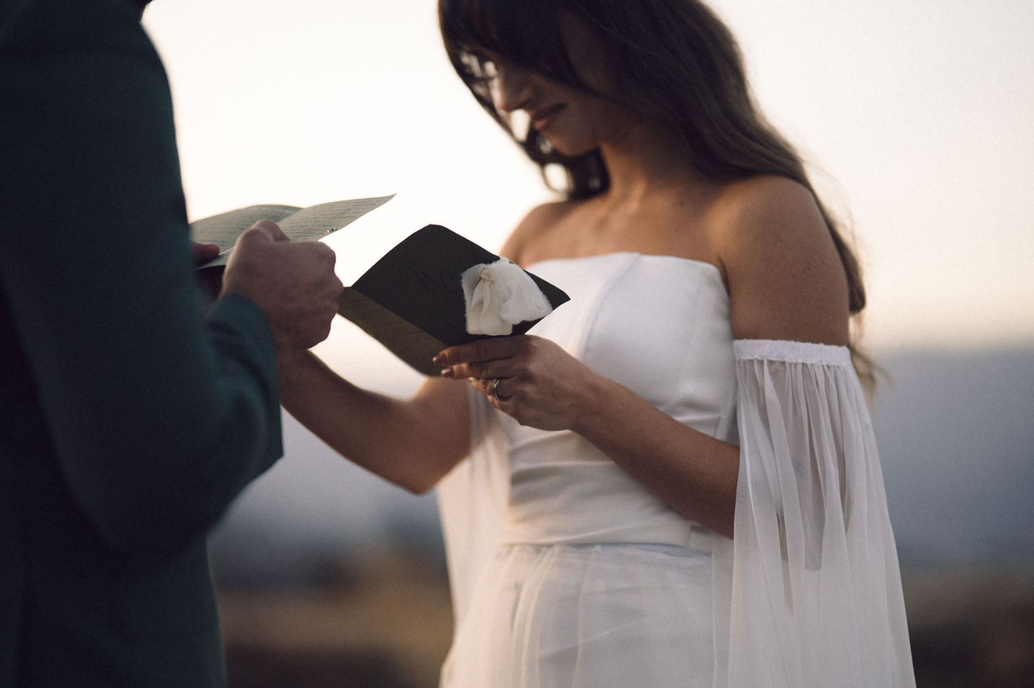 Bride in a flowing white dress stands in golden sunlight during a romantic outdoor photoshoot.