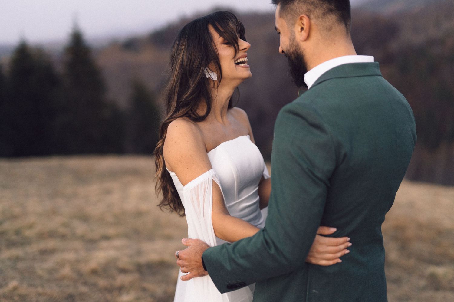 A couple in wedding attire embraces during a romantic outdoor photo session in a mountainous landscape.