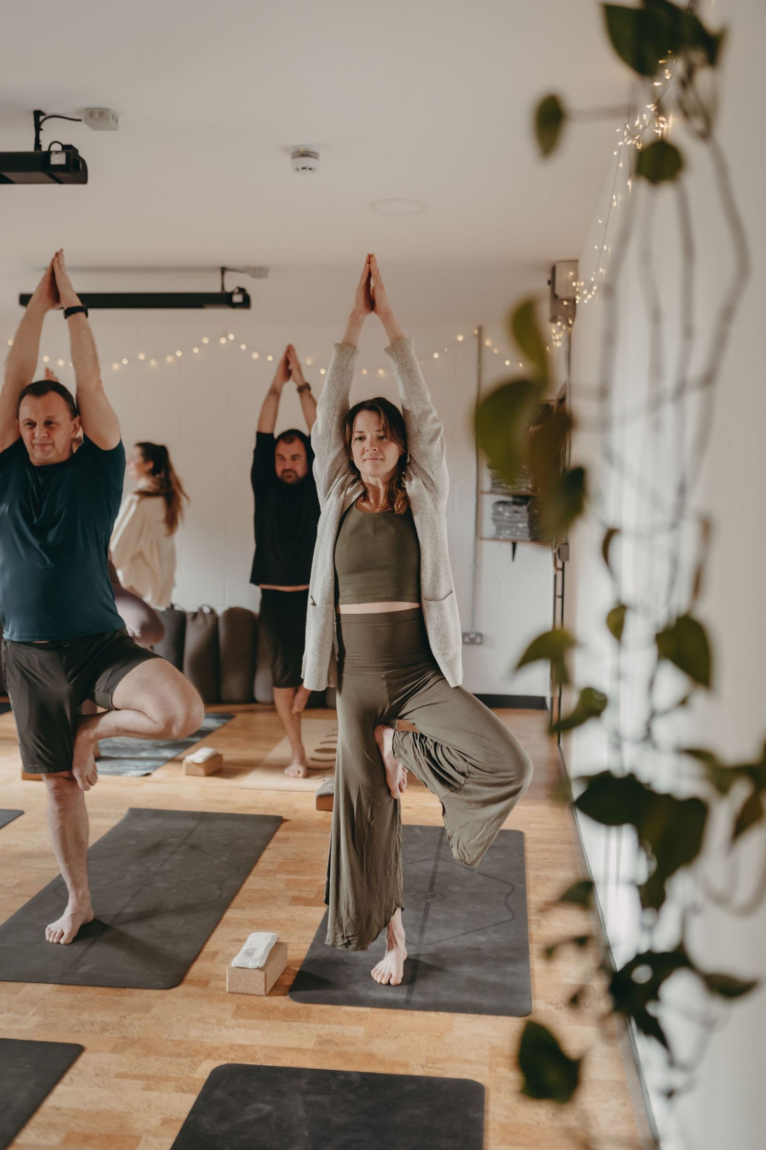 A person performs a series of stretching exercises on a yoga mat in a minimalist studio space with white walls and wooden floors.