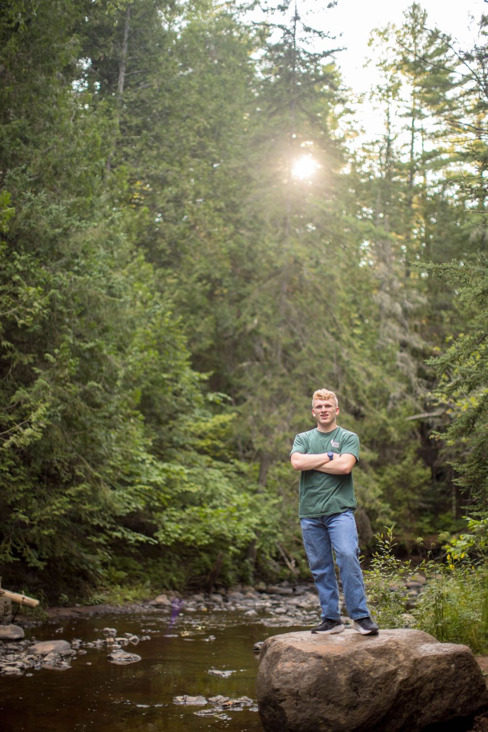 A person poses near a tranquil forest stream with sunlight filtering through evergreen trees in multiple shots.