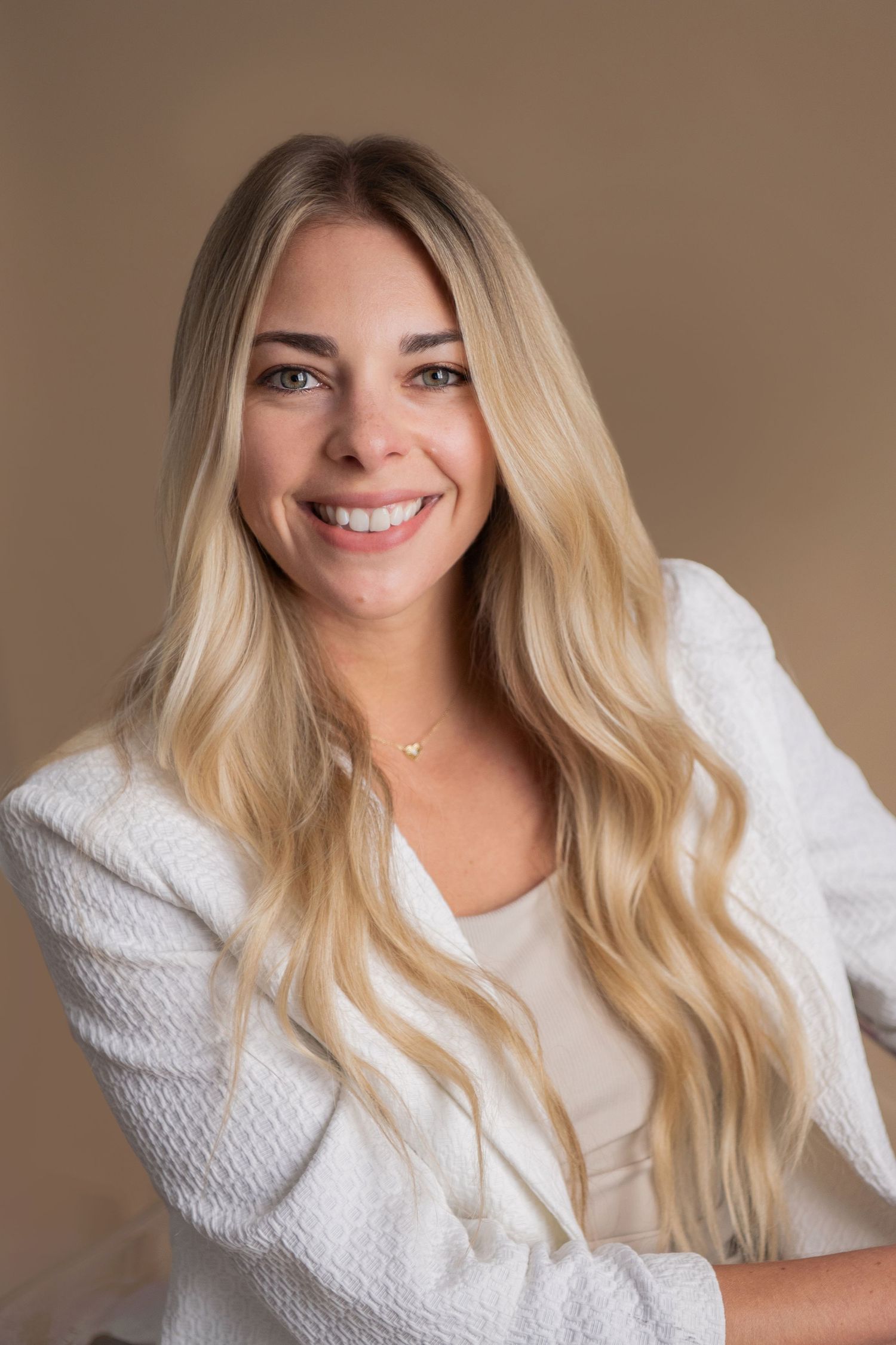 Professional portrait of someone with long wavy blonde hair wearing a white sweater against a neutral background.
