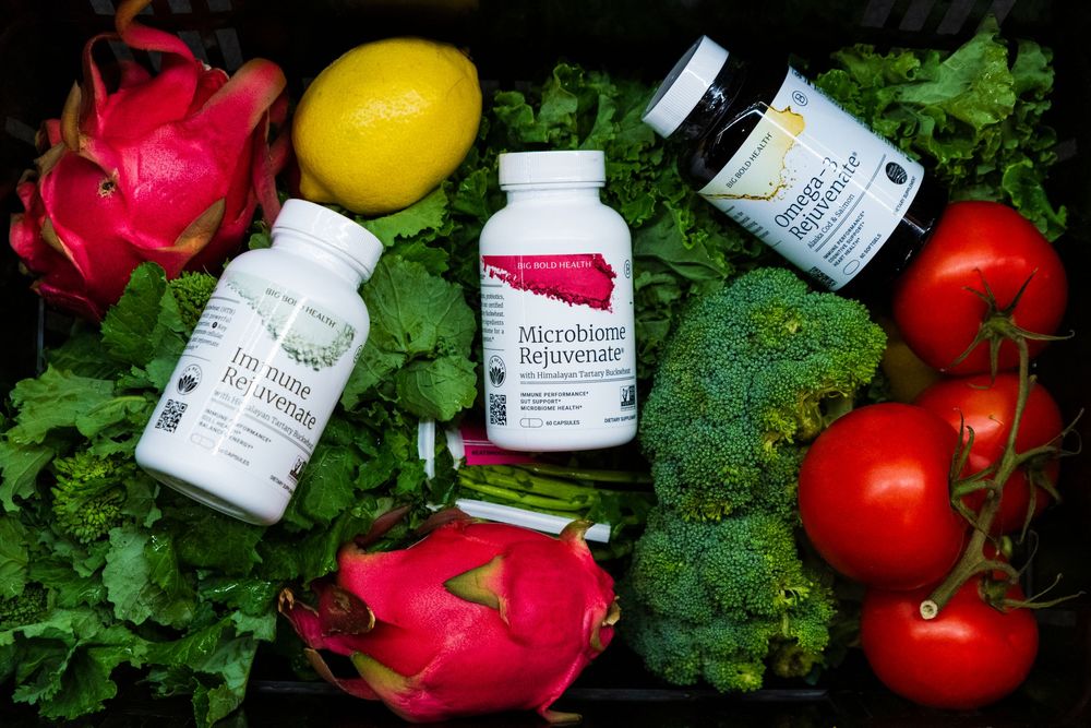 Fresh produce and skincare products arranged with tomatoes, broccoli, and white cosmetic bottles against green foliage.