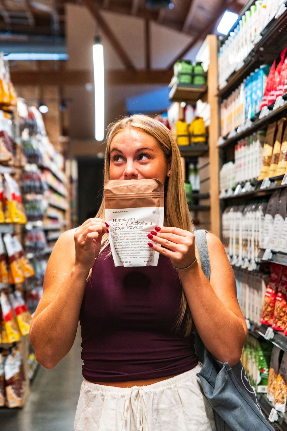 Customer examining product labels while shopping in a grocery store aisle with a gray tote bag.
